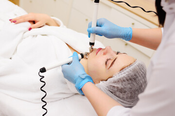 cosmetologist conducts microcurrent facial therapy for a young woman using a device in a beauty...