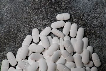 Big pile of white pills on rustic concrete like background. with negative space for text.