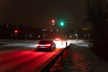 Two cars driving over the intersection in a snowstorm at night