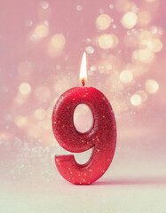 Uma vela vermelha, de aniversário, acesa, com o número nove com glitter dourado e fundo cor-de-rosa e brilhos em bokeh.