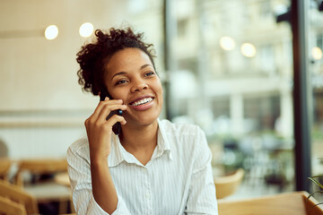 A smiling African woman making a phone call, sitting at the cafe.
