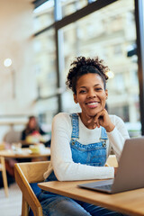 A smiling curly-haired woman, working online, sitting at the cafe.