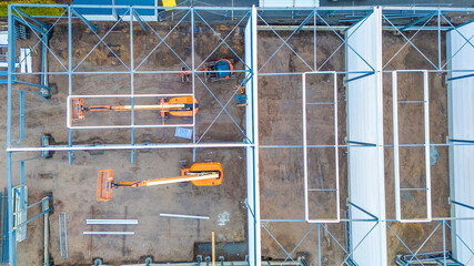 This aerial image provides a bird's-eye view of a construction site, showcasing the geometric arrangement of scaffolding and machinery. Two orange telescopic boom lifts stand out against the muddy © Bjorn B