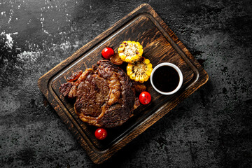 Grilled Ribeye Steak on bones on wooden board, prime cowboy steak on dark background