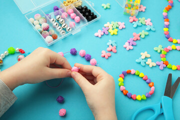 Little girl made bracelets on blue background. Kids handmade beaded jewelry. DIY bracelet beads.