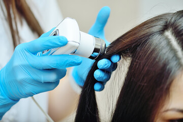 doctor cosmetologist dermatologist diagnoses the condition of the patient's hair using a special device - a trichoscope. - obrazy, fototapety, plakaty