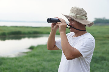 Handsome Asian man ecologist is surveying nature at the lake, hold binoculars. Concept, nature...