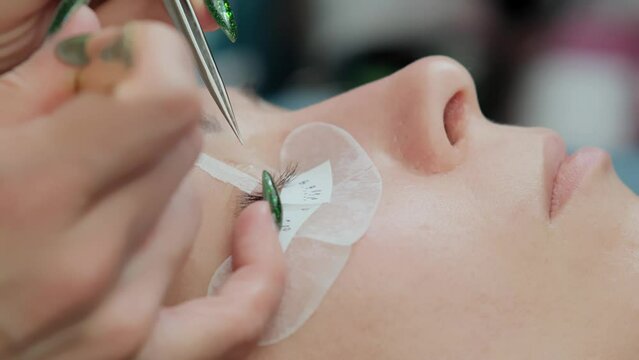 Close-up of eyelash extension procedure. Work process of a professional beauty technician lengthening women's eyelashes. False eyelashes. Eyelash extensions close-up. 