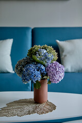 Hydrangeas in vase on table with blue sofa background.