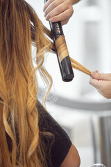 Stylist curling long blonde hair with a curling iron