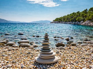 Zelfklevend Fotobehang Small cairn from beach rocks, with beautiful landscape of Croatia behind, Croatia coast, sea and rocks in water. © Alexandr