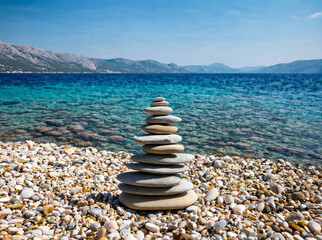 Fototapeta na wymiar Small cairn from beach rocks, with beautiful landscape of Croatia behind, Croatia coast, sea and rocks in water.