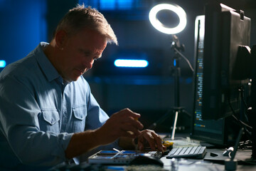 Mature Male Electronics Expert Repairing Laptop In Workshop With Low Key Lighting