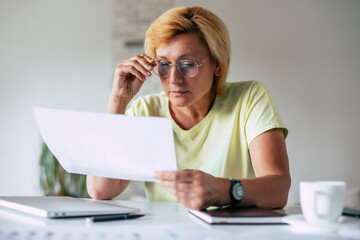 Close up portrait of clever middle-aged woman in goggles with papers while sitting by workplace in...