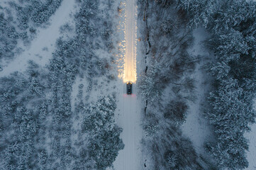 A car in the middle on the snowy country road between forest. View from above