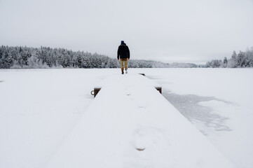 Man walking on wooden board walk in frozen lake