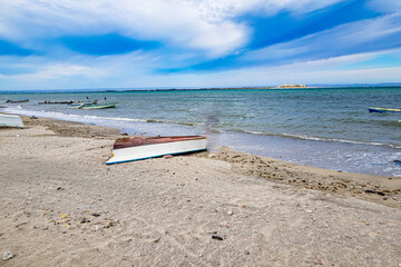 Seascape on coastal beach, boat overturned on sand, others in waters of Sea of Cortez, peninsula...