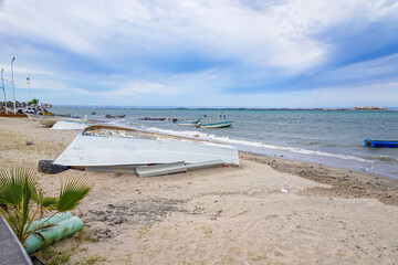 Boats overturned on sand on coastal beach, others in waters of Sea of Cortez, seascape with peninsula and horizon against blue sky with white clouds in background, La Paz, Baja California Sur Mexico