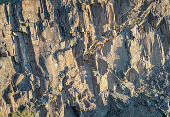 Fototapeta premium View of Spectacular vertical walls cliffs of Salisbury Crags. Crumbling rock cliff wall texture with cuts and shadows of The granite rock, Nature stone background, Space for text, Selective focus.