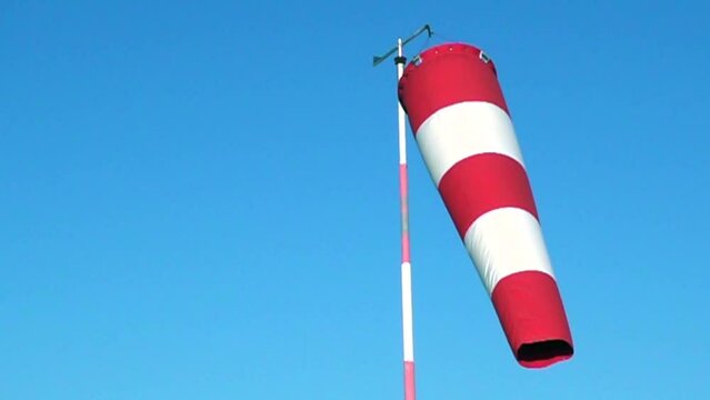 video of a wind sleeve to signal wind direction and intensity positioned at a small parachute airfield, isolated against a blue sky