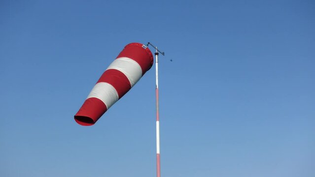 video of a wind sleeve to signal wind direction and intensity positioned at a small parachute airfield, isolated against a blue sky