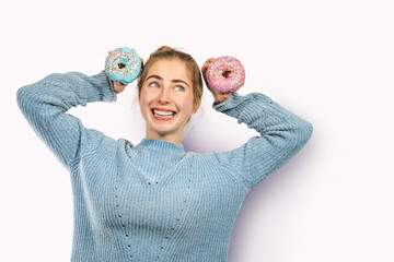 Excited crazy happy young european girl showing donuts isolated pastel pink background has sweet tooth breaks diet. Junk food concept