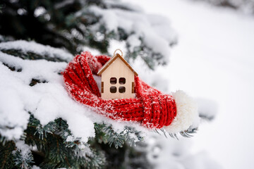 Naklejka premium A house in a red scarf on a branch of a fir tree in the snow in winter in the park. Concept of winter, Christmas, new year, warm, cozy, loving, protecting
