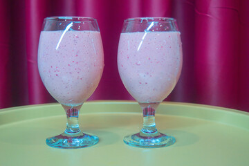 Two glasses with banana-strawberry smoothie on a table against the background of burgundy curtains close-up.