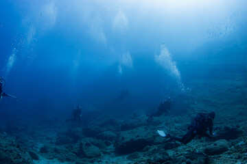 Divers over massive volcanic blocks in blue water on a dive in Mauritius