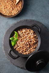 Buckwheat porridge with fresh herbs in a black pan on a board on a dark  background with raw grains.