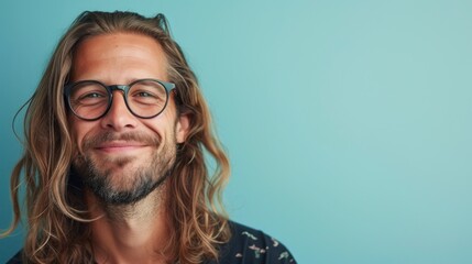 Smiling man with long hair and glasses against a light blue background.