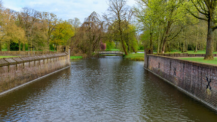 Stone embankment channels in the  idyllic De Haar Castle park canal. Spring green trees. Utrecht, Netherlands.