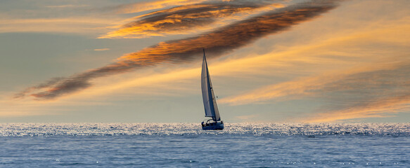 Silhouette of a sailboat sailing towards the horizon through the Mediterranean Sea