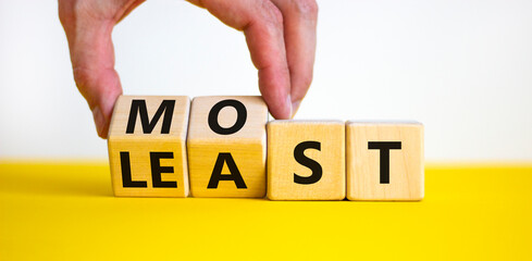 Most or least symbol. Businessman turns beautiful wooden cubes and changes the word Least to Most. Beautiful yellow table white background. Copy space. Business and most or least concept.