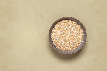 Uncooked oat flakes in a bowl on a light plaster background. Top view, copy space.