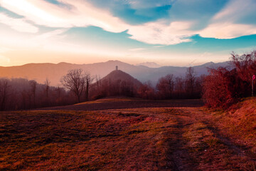 Country landscape at sunset with ancient tower, mountains and white clouds.
