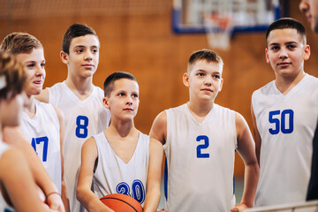 A junior basketball players standing on court and listening coach.