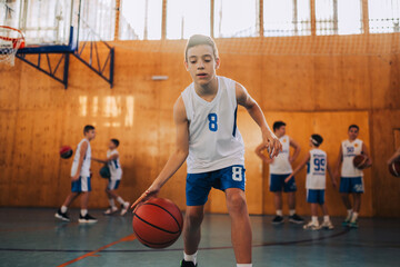 A young basketball kid is dribbling a ball and practicing at court.