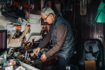 An old craftsman is gluing shoes at how workshop.