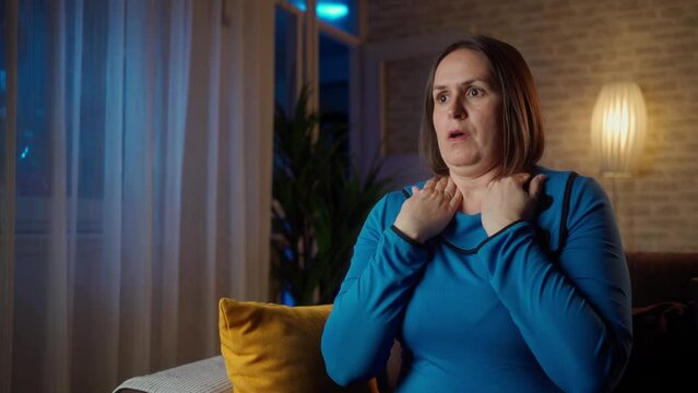 Mature woman alone at home with a panic attack shortness of breath, trembling, numbness, loss of consciousness. Front view of a female suffering an anxiety sitting on a couch. chest pain, fear symptom