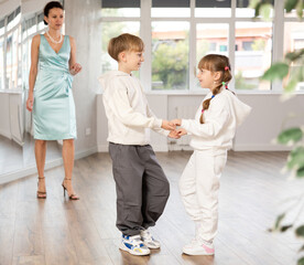 Boy and girl kids in sport wear repeat movement while taking rumba dancing lessons. Female teacher...