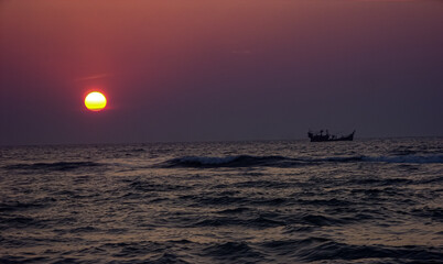 sun is sitting in the sea level and a boat is passing through