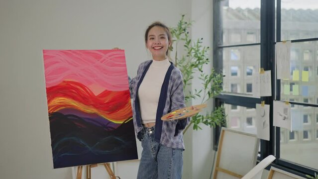 Innovative asian female painter using red paint on big canvas,holding tube of oil paint,fine art artist drawing,Abstract acrylic painting in the art studio.asian woman painting brush on canvas