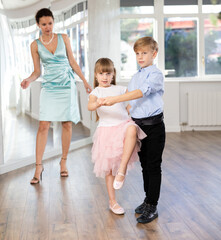 Boy paired up with girl during contemporary dancing lesson. Children rehearse hustle while female...