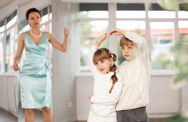 Fototapeta premium Boy paired up with girl during contemporary dancing lesson. Children in sport wear rehearse hustle while female teacher conduct dance class