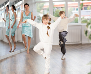 Fototapeta premium Cheerful preteen girl and boy enjoying modern dancing during lesson in dance studio, practicing hip-hop movements under guidance of female teacher..