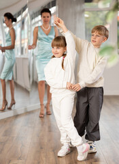 Passionate tween dancers, girl and boy practicing ballroom dancing in dance studio, gracefully performing waltz while female trainer monitoring technique and progress..