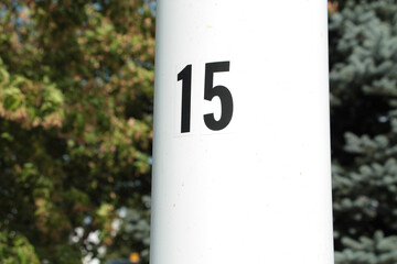 number 15 on white metal clean white post pole thick in black with tree behind blurred exterior...