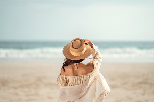 Summer beach vacation concept, Young woman with hat relaxing with her arms raised to her head enjoying looking view of beach ocean on hot summer day, copy space.