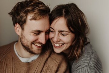 Happy couple embracing and laughing together against a neutral background.
